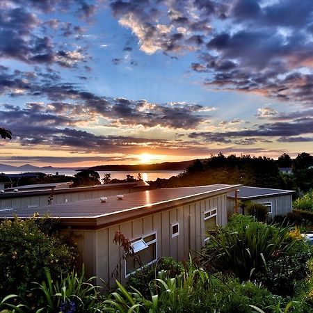 Taupo Debretts Spa Resort Екстер'єр фото The photo depicts a serene landscape during sunset. In the foreground, there is a modest building partially covered by greenery. The roof of the building is visible, along with some windows. Surrounding the structure are lush plants and foliage. 

In
