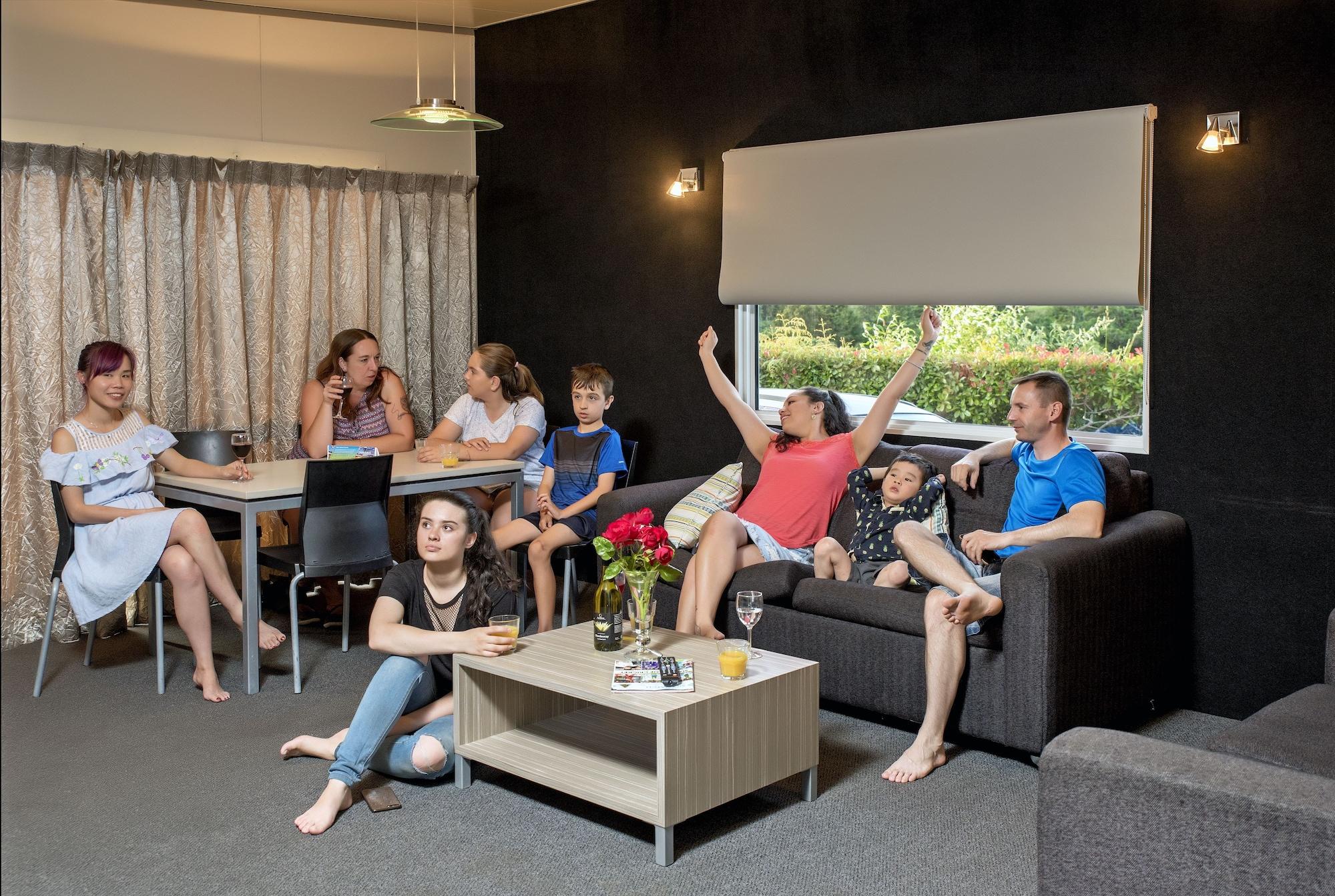 Taupo Debretts Spa Resort Екстер'єр фото The photo shows a group of people gathered in a cozy living room. There are several adults and children interacting with each other. One woman in a red top appears to be celebrating or expressing excitement, while others are engaged in conversation o