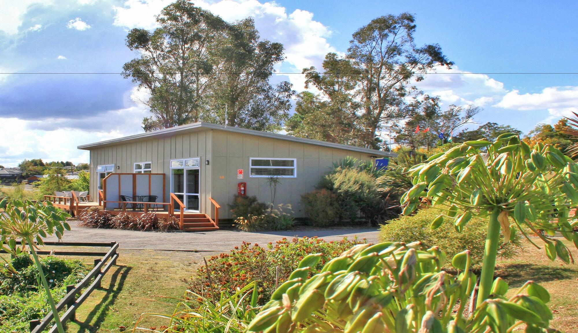 Taupo Debretts Spa Resort Екстер'єр фото The image shows a small, modern building surrounded by greenery. The structure has a light-colored exterior with large windows and a ramp leading up to the entrance. In front of the building, there is a landscaped area with various plants and flowers