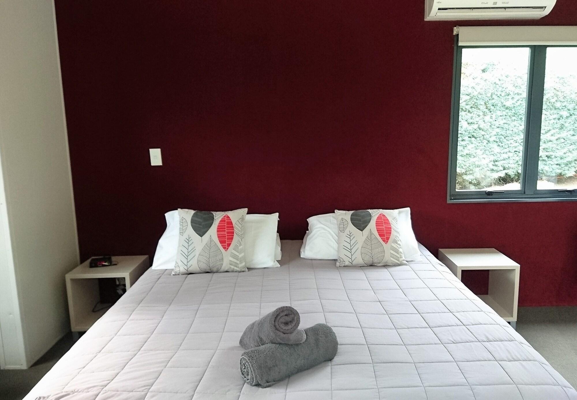Taupo Debretts Spa Resort Екстер'єр фото The photo shows a cozy bedroom featuring a large bed with a light-colored quilt. The bed has two decorative pillows with a simple design on each side. There are two bedside tables, one on each side of the bed. On the bed, there are rolled towels plac