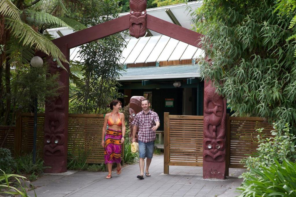 Taupo Debretts Spa Resort Екстер'єр фото The photo depicts a welcoming entrance, marked by a decorative archway featuring traditional cultural carvings. Two individuals are walking through the entrance: one is a woman wearing a vibrant, patterned dress, and the other is a man dressed casual