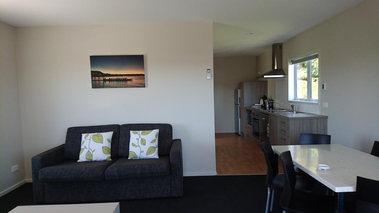Taupo Debretts Spa Resort Екстер'єр фото The photo shows a modern living space that includes a living area and a kitchen. The living area features a dark sofa with two decorative pillows that have a leaf pattern. There is a framed picture on the wall, depicting a scenic view, possibly of a 