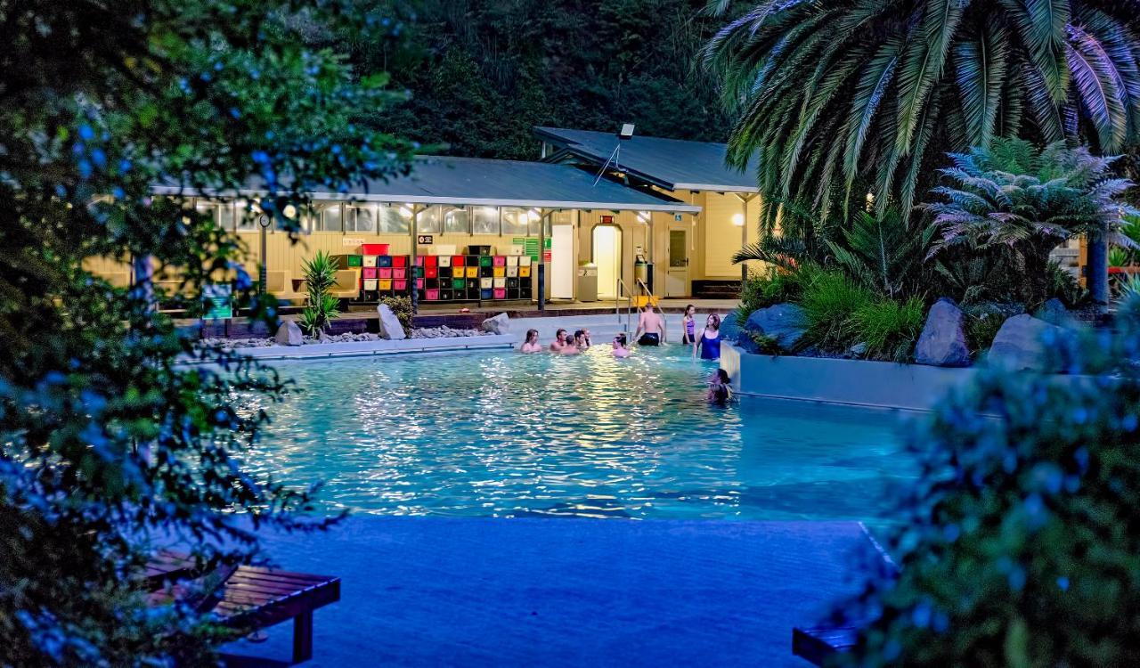 Taupo Debretts Spa Resort Екстер'єр фото The photo shows a scenic pool area illuminated by soft lighting during the evening. People can be seen enjoying the water, suggesting a relaxed atmosphere. In the background, there's a building with large windows, which appears to be part of a facili