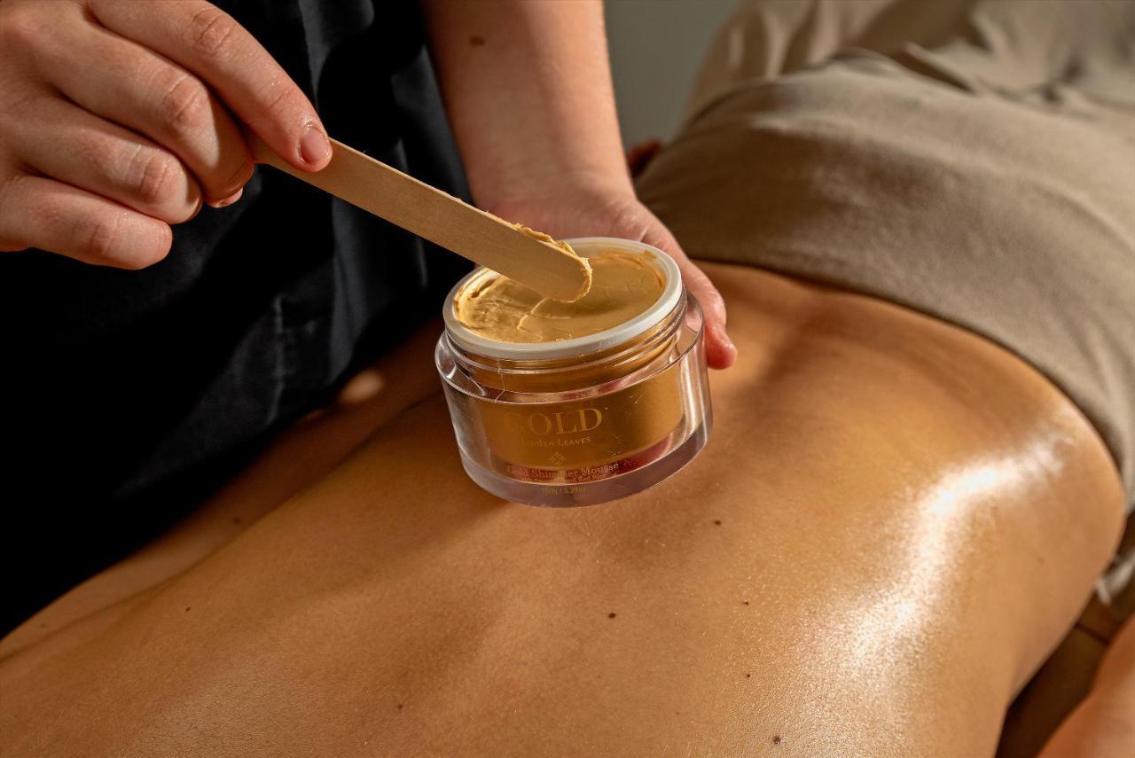 Taupo Debretts Spa Resort Екстер'єр фото The photo shows a close-up of a back, likely during a spa or beauty treatment. A person is using a wooden spatula to apply a golden-colored substance from a jar to the skin. The jar is clear and labeled, and the skin appears smooth and slightly gloss