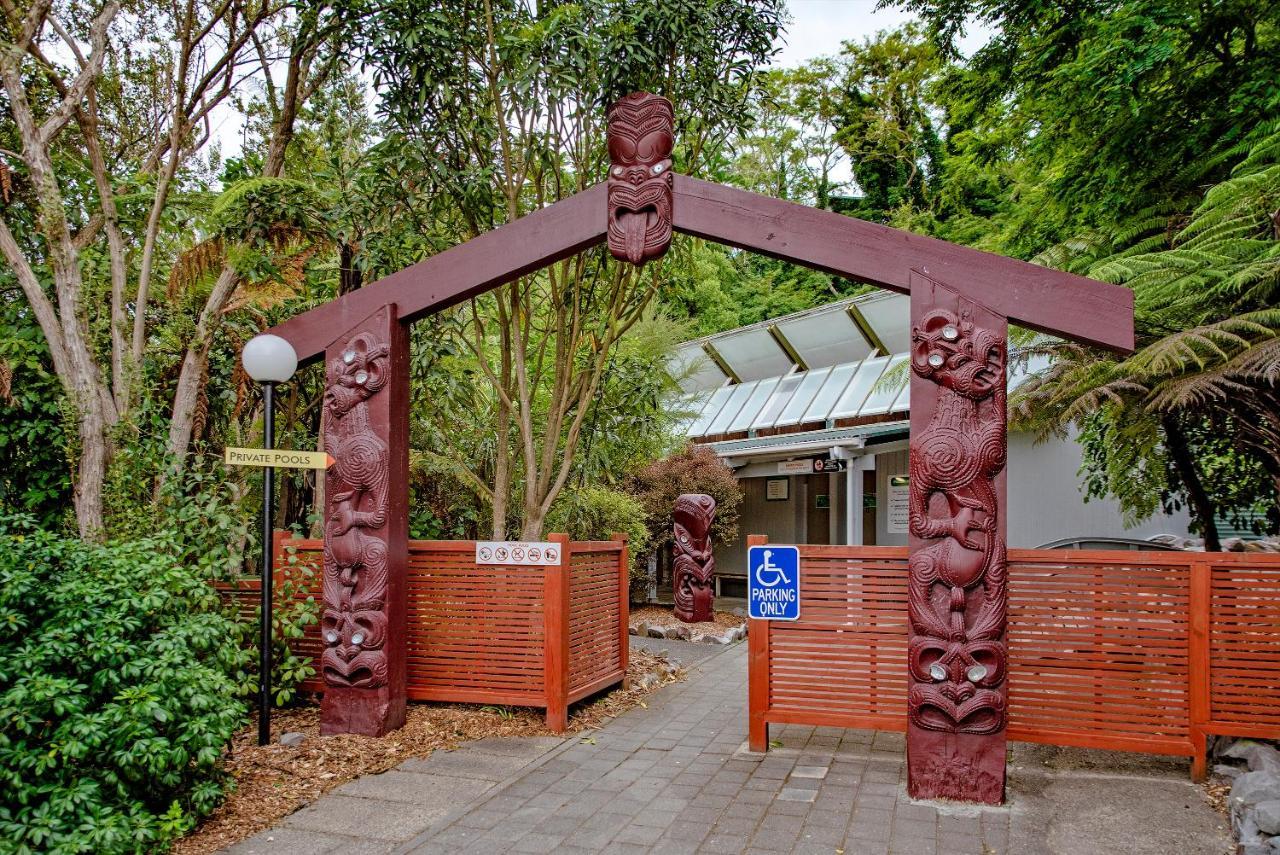 Taupo Debretts Spa Resort Екстер'єр фото The photo shows an entrance with a large archway that features intricate carvings. The arch is supported by two vertical posts, each adorned with detailed figures likely representing cultural symbols or characters. Surrounding the entrance are lush g