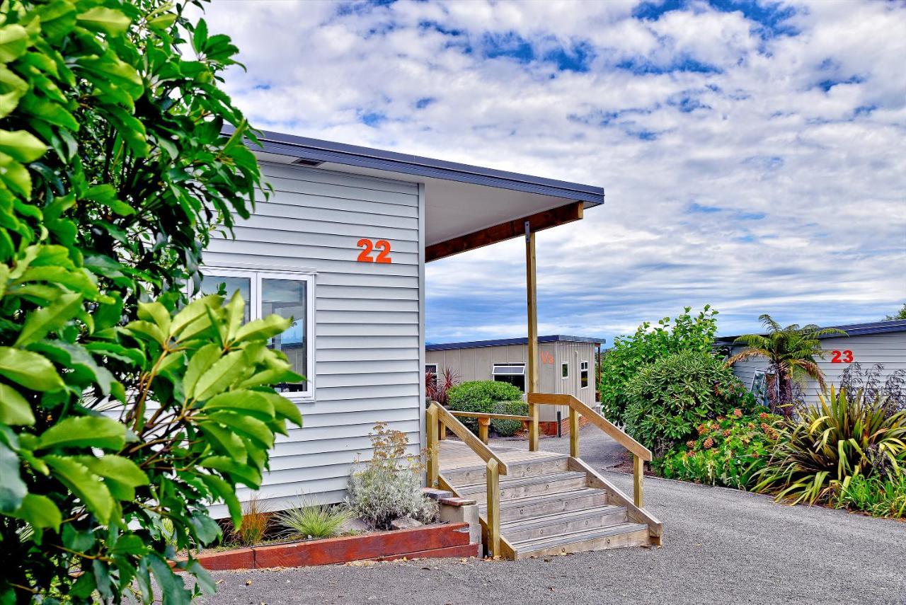 Taupo Debretts Spa Resort Екстер'єр фото The photo shows a building, likely a cabin or cottage, with a wooden porch and stairs leading up to it. The structure has light-colored siding and the number "22" is prominently displayed on the side. Surrounding the building are various plants and t