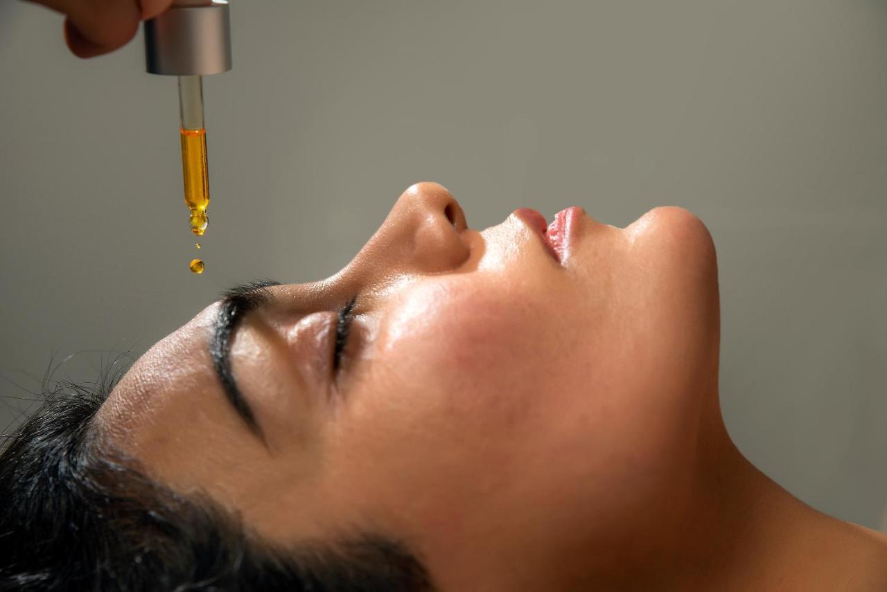 Taupo Debretts Spa Resort Екстер'єр фото The image shows a close-up of a woman's face as she lies back, eyes closed. A dropper is held above her forehead, with a drop of an oil or serum about to fall. The woman's skin appears radiant and moist, indicating a skincare treatment, possibly focu