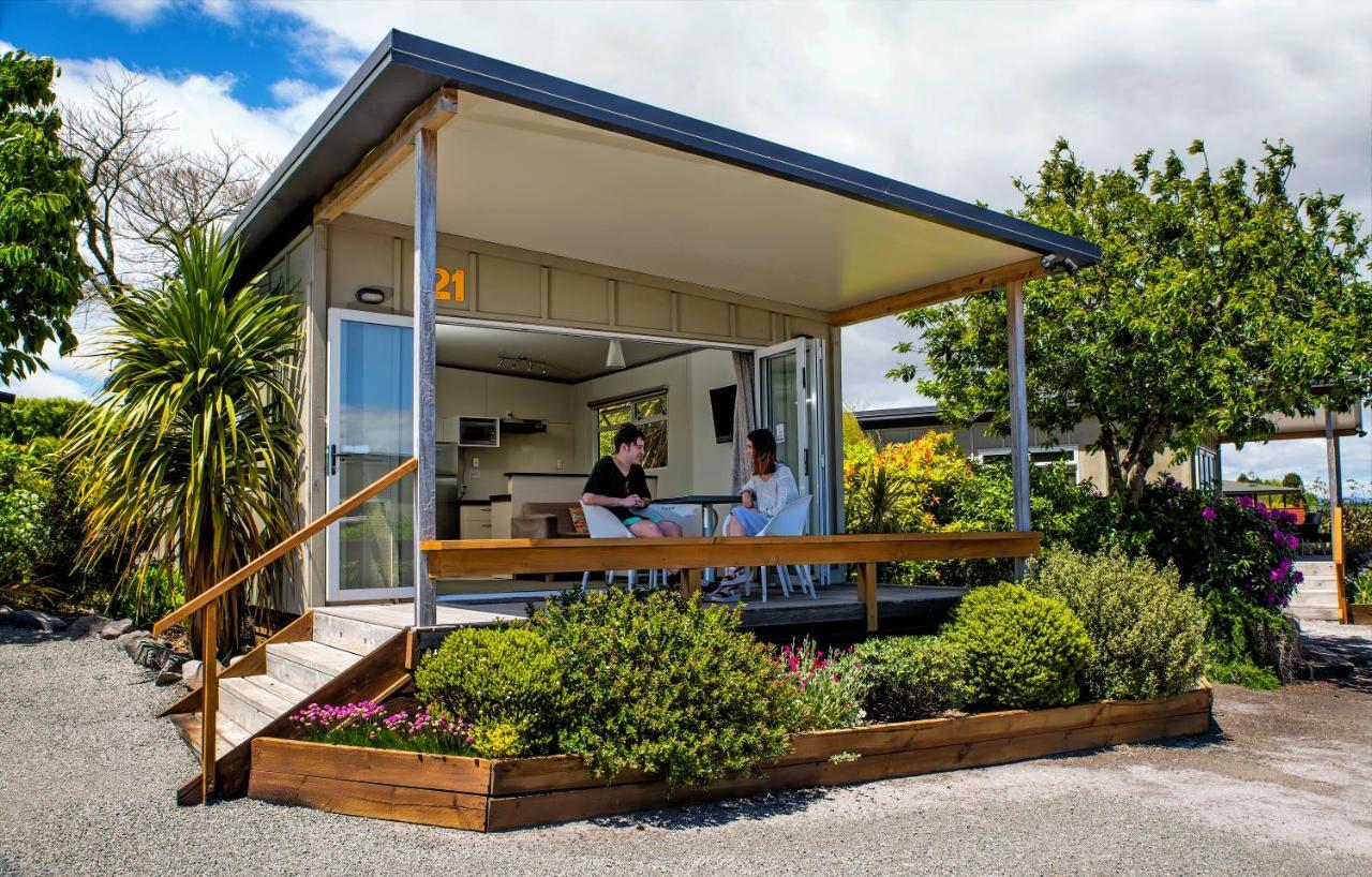 Taupo Debretts Spa Resort Екстер'єр фото The photo depicts a modern small house or cabin, featuring a covered porch with a wooden railing. Two people are seated at a table on the porch, engaging in conversation. The exterior of the house is designed with large windows, allowing ample natura